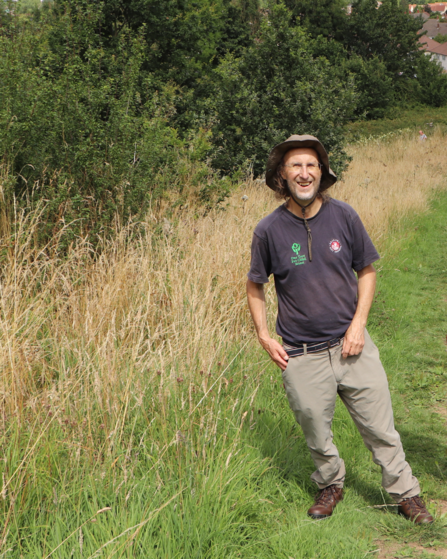 Bob, a WildCAT volunteer, standing in a field with trees behind him