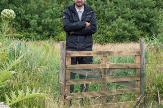 John stands besides a gate on a reserve